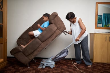 shot-of-a-grandmother-vacuuming-under-a-couch-whic-2023-11-27-05-20-29-utc