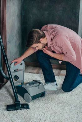 young-man-looking-at-broken-vacuum-cleaner-at-home-web
